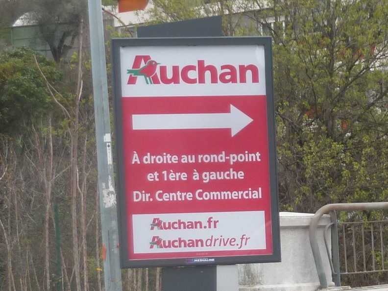 Panneau publicitaire 2 m² exploité par Espaces Conseils, en abord de rond-point, portant une campagne directionnelle Auchan